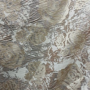 May include: A white fabric with a textured, embossed pattern in a light brown color. The pattern resembles a floral design.