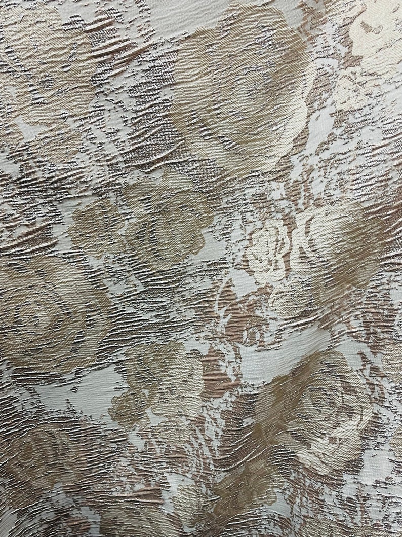 May include: A white fabric with a textured, embossed pattern in a light brown color. The pattern resembles a floral design.