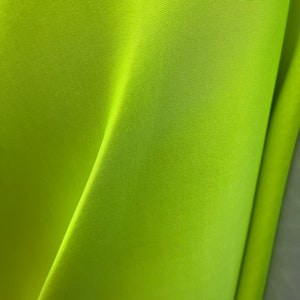 May include: A bright neon green fabric with a smooth, slightly textured surface. The fabric is folded in half, creating a sharp crease.