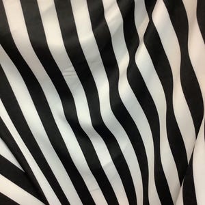 Könnte beinhalten: Schwarz-weiß gestreiftes Stoff mit einer glatten, seidenartigen Textur. Der Stoff ist gefaltet und drapiert, wodurch die Streifen diagonal verlaufen.