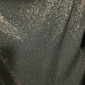 May include: Black fabric with a silver glitter pattern. The fabric has a subtle texture and a slightly iridescent sheen.
