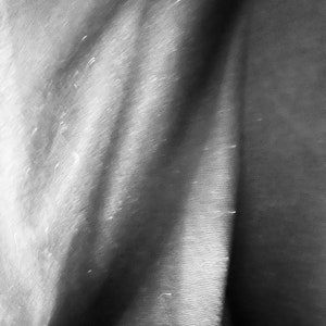 May include: A close-up of a textured, gray fabric with a soft, flowing drape. The fabric is folded and has a subtle sheen.