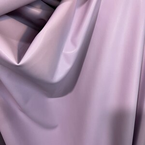 K&ouml;nnte beinhalten: Nahaufnahme eines weichen, glatten, helllila Stoffes. Der Stoff ist gefaltet und drapiert, wodurch seine Textur und Farbe sichtbar werden.