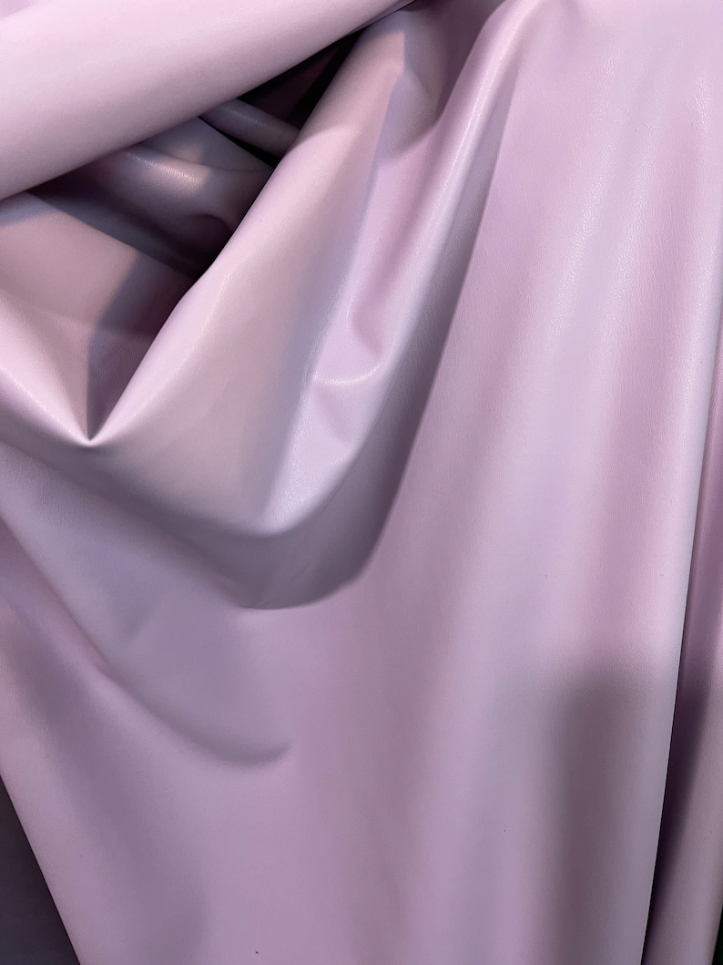 K&ouml;nnte beinhalten: Nahaufnahme eines weichen, glatten, helllila Stoffes. Der Stoff ist gefaltet und drapiert, wodurch seine Textur und Farbe sichtbar werden.