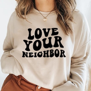 Può includere: Una felpa beige con la scritta "LOVE YOUR NEIGHBOR" stampata in lettere retrò nere.