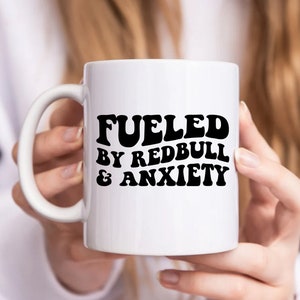 Puede incluir: Taza de cer&aacute;mica blanca con texto negro que dice "Fueled by Redbull & Anxiety".
