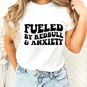 Puede incluir: Camiseta blanca con texto negro que dice "Fueled by Redbull & Anxiety".