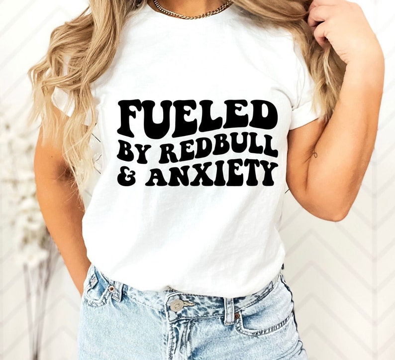 Puede incluir: Camiseta blanca con texto negro que dice "Fueled by Redbull & Anxiety".