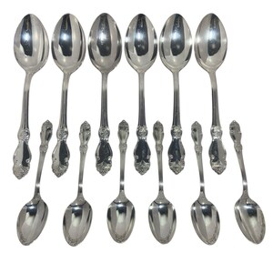 May include: A collection of silver spoons and smaller teaspoons. The spoons have a classic design with ornate detailing on the handles. The spoons are arranged on a white background, reflecting light.
