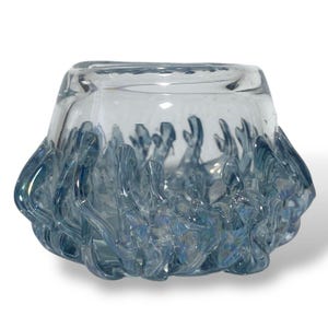 May include: A clear glass bowl with a light blue, textured, wave-like design around the bottom edge. The bowl has a rounded shape and a smooth interior. The blue design has an iridescent quality, reflecting light.