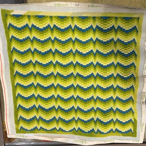 May include: A needlepoint canvas with a repeating wave pattern in shades of green and blue. The design features a gradient effect, with lighter greens at the top and darker blues at the bottom. The canvas is labeled "2 Stitcherie TOP".