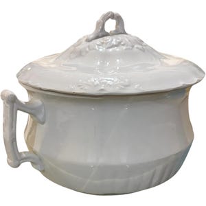 May include: White ceramic serving dish with a lid and handle. The dish has a rounded body with a handle on the side and a decorative handle on the lid. The lid has a floral design. The dish is likely for serving food.