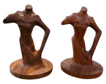 May include: Two wooden sculptures of abstract figures with a smooth, brown finish. The figures are stylized and have a modern design.