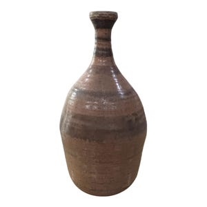 May include: A handcrafted, brown ceramic vase with a narrow neck and a rounded body. The vase features horizontal bands of varying shades of brown and tan, creating a textured appearance. The vase is a decorative item.