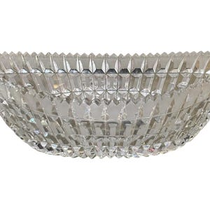 May include: A clear, faceted glass bowl with a diamond pattern. The bowl has a wide, oval shape and is made of clear glass. The edges of the bowl are also faceted, creating a sparkling effect. This decorative bowl is ideal for serving or display.