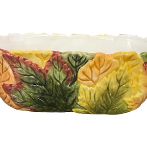 May include: An oval ceramic serving bowl with a white interior and an exterior design of colorful autumn leaves. The leaves are in shades of green, yellow, orange, and red.