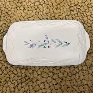 May include: A rectangular white serving platter with a floral design. The platter features embossed wheat stalks and a central design of purple, pink, and green flowers and leaves. The platter has two handles.