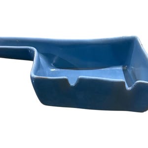 May include: A light blue ceramic ashtray with a rectangular shape and a handle. The ashtray has a smooth, glossy finish and a small notch for resting cigarettes. The handle extends from the side.