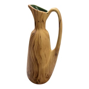 May include: A wooden pitcher with a green glazed top and a wood grain pattern. The pitcher has a wide base and a narrow neck.