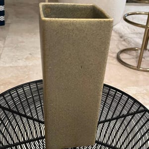 May include: A square, light green ceramic vase with a textured surface.