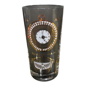 May include: A tall, clear glass with a dark gray tint. The glass features a gold and white clock design with the text "ROME 11 A.M." and other decorative elements. The clock shows the time as 3 A.M.