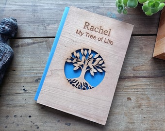 Puede incluir: Un diario de madera con un borde azul y un diseño de árbol de la vida recortado. El diario está personalizado con el nombre "Rachel" y el texto "My Tree of Life".