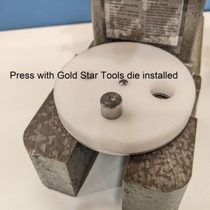 May include: A white press with a round white die and a silver die installed. The press has a gray metal base and a black handle. The text "Press with Gold Star Tools die installed" is visible on the image.