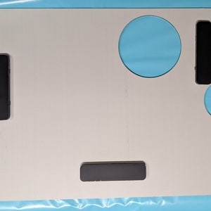 May include: A white plastic tray with three black rectangular magnets and a circular cutout. The tray has a wavy edge on the right side.