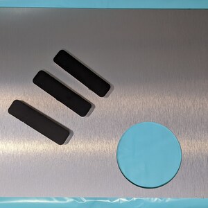 May include: A brushed silver metal plate with three black rectangular cutouts and a round cutout. The plate has a brushed finish.