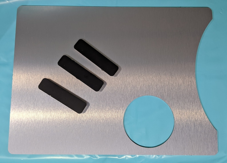 May include: A brushed silver metal plate with three black rectangular cutouts and a round cutout. The plate has a brushed finish.