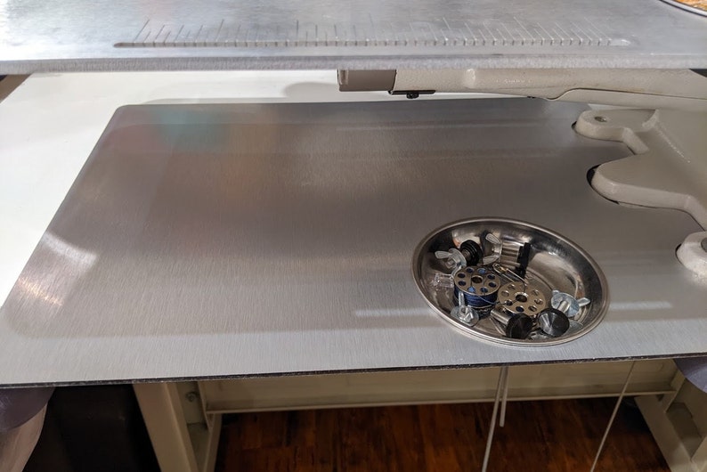 May include: A silver metal sewing machine table with a small metal bowl filled with sewing machine parts.
