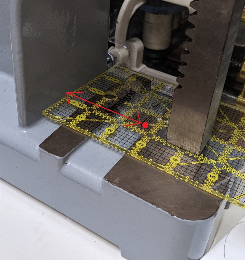 May include: A yellow Omnigrid ruler with a grid pattern is positioned on a gray metal surface. The ruler is being pressed down by a metal bar.