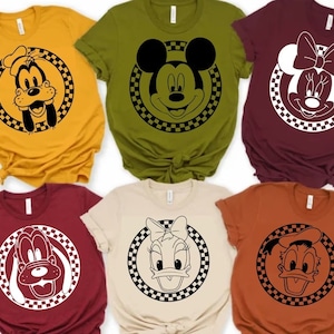 May include: Six different t-shirts featuring various Disney characters in black and white. The characters are Mickey Mouse, Minnie Mouse, Donald Duck, Goofy, and Daisy Duck. Each character is surrounded by a checkered circle.