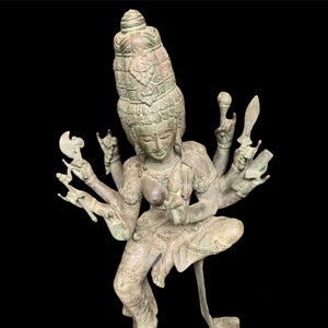 Puede incluir: Una estatua de bronce verde de una deidad hindú con múltiples brazos, cada uno sosteniendo un objeto diferente. La deidad lleva una corona y joyas elaboradas.