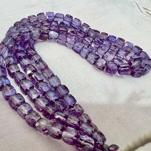 May include: Strands of faceted, purple beads. The beads are a mix of light and dark purple hues, with a slightly translucent quality. The beads are strung together, forming multiple rows. The beads are a mix of light and dark purple hues.