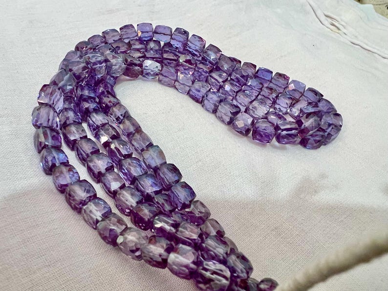 May include: Strands of faceted, purple beads. The beads are a mix of light and dark purple hues, with a slightly translucent quality. The beads are strung together, forming multiple rows. The beads are a mix of light and dark purple hues.