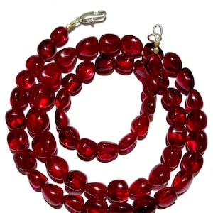 May include: A strand of red gemstone beads with a silver clasp. The beads are oval shaped and have a glossy finish.