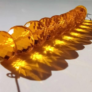 May include: A strand of amber-colored faceted glass beads. The beads are strung on a silver wire and have a shiny, reflective surface.