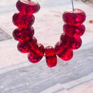 Peut inclure: Un brin de perles de verre facettées rouge foncé enfilées sur un fil d'argent.