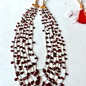 Könnte beinhalten: Eine mehrreihige Halskette aus roten Edelsteinperlen mit einem Silberdraht und einem goldenen Quastenanhänger.