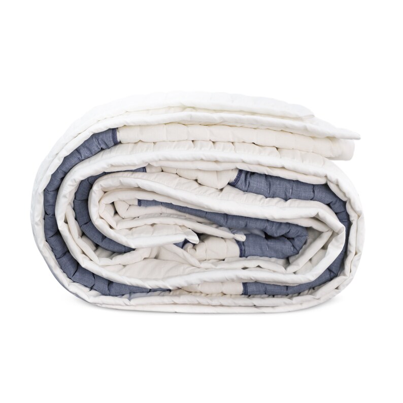 A white and blue quilted blanket rolled up. The blanket has a white background with blue stripes and is made of a soft, textured fabric.