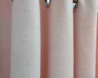 Puede incluir: Primer plano de cortinas rosa pálido con ojales plateados colgadas de una barra de madera. La tela tiene un aspecto texturizado, creando un ambiente acogedor y acogedor. Las cortinas están parcialmente corridas.