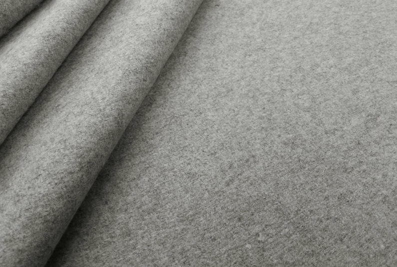 A detailed close-up of a light gray solid wool felt curtain, showcasing the high-quality 2mm thick premium felt texture. The soft, dense natural fiber material provides superior thermal insulation & energy-saving properties for cold winter months. Perfect for custom home decor, this durable gray wool fabric adds a minimalist and modern look to luxury window treatments. Ideal as sound-reducing drapes for a home office, dorm room, or designer bedroom, providing a sophisticated & cozy tactile feel.