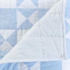 May include: A white and light blue patchwork quilt with a diamond pattern. The quilt is folded in half, revealing the white cotton lining.