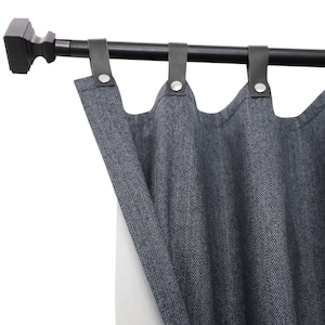 May include: Gray herringbone patterned curtains hanging from a black metal curtain rod with black leather tabs.