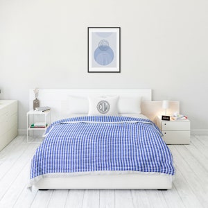 May include: A white bed with a blue and white gingham duvet cover. The bed has a white headboard and a white pillow with the letters "EDW" in a circle. There is a white bedside table with a lamp and a clock on it.