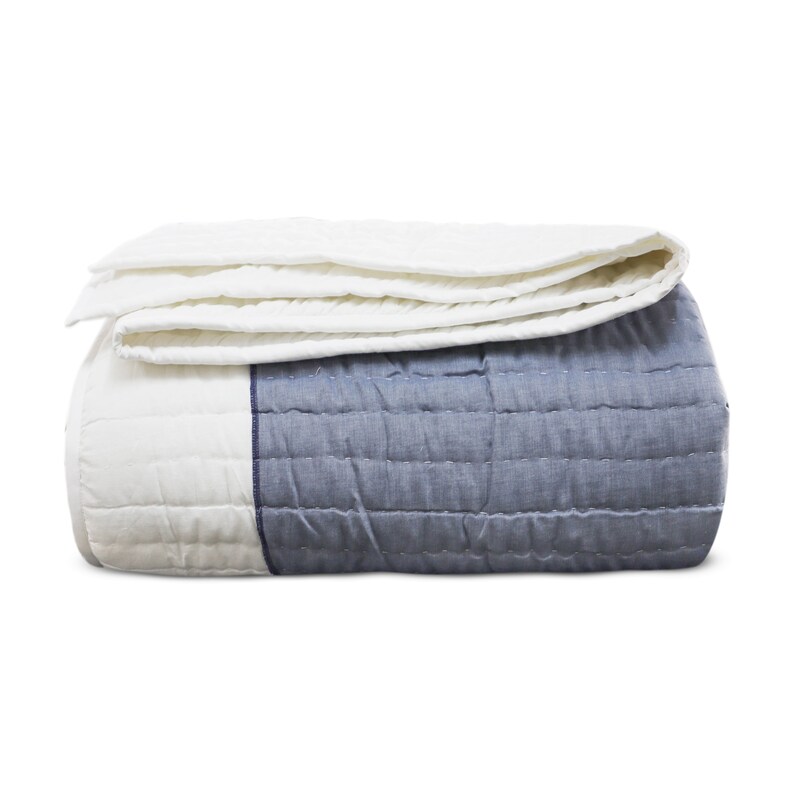 A folded white and blue quilt with a quilted pattern. The quilt is folded in thirds with the white side on top and the blue side on the bottom.