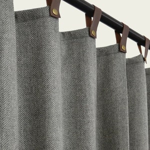 Puede incluir: Cortinas grises con patrón de espiga, pestañas de cuero marrón y anillos de latón colgando de una barra de cortina negra.