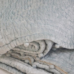 This close-up highlights the plush texture of the blue-gray velvet pick stitch quilt. The medium-weight handmade blanket is filled with soft cotton batting, functioning as a warm bed quilt or lap quilt. Available in custom sizes from crib quilt to king size quilt, it serves as a high-quality baby shower gift or a stylish twin quilt for students. The tonal depth and pom pom quilt trim make it a standout piece for a bohemian or modern bedding set.
