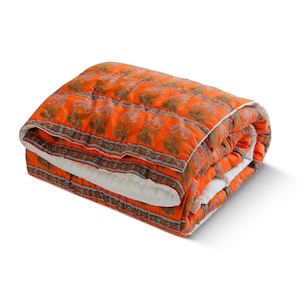 Puede incluir: Edredón naranja plegado con un estampado floral en tonos marrones y verdes. El edredón tiene un reverso blanco y un borde decorativo con detalles azules. El edredón está hecho de un material suave y acolchado.